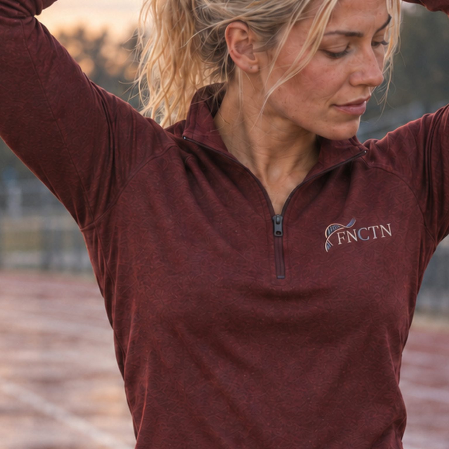 Close on the zip and FNCTN embroidery of the Maroon Quarter Zip, arms raised at the track