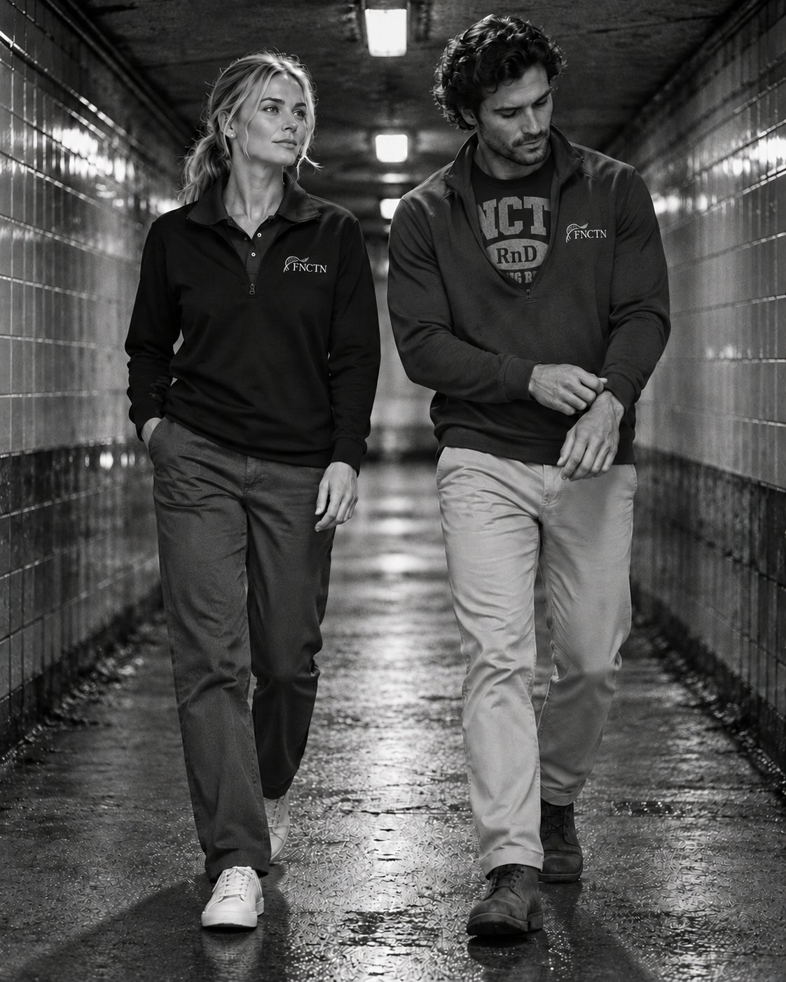 Two people walking a tiled underpass, the Black quarter zip over the Navy polo and over the Varsity Tee